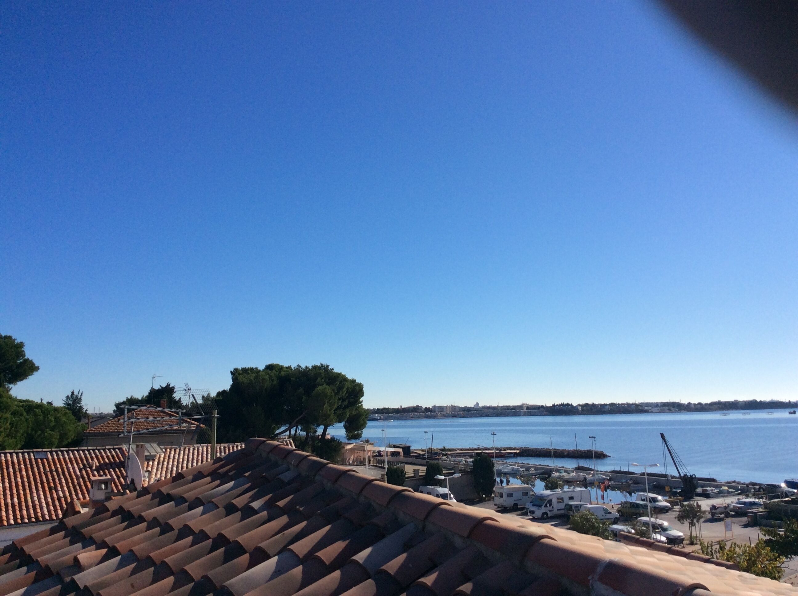 Un port de plaisance sur la côte, avec des bateaux, un ciel bleu dégagé et un toit en tuiles au premier plan.