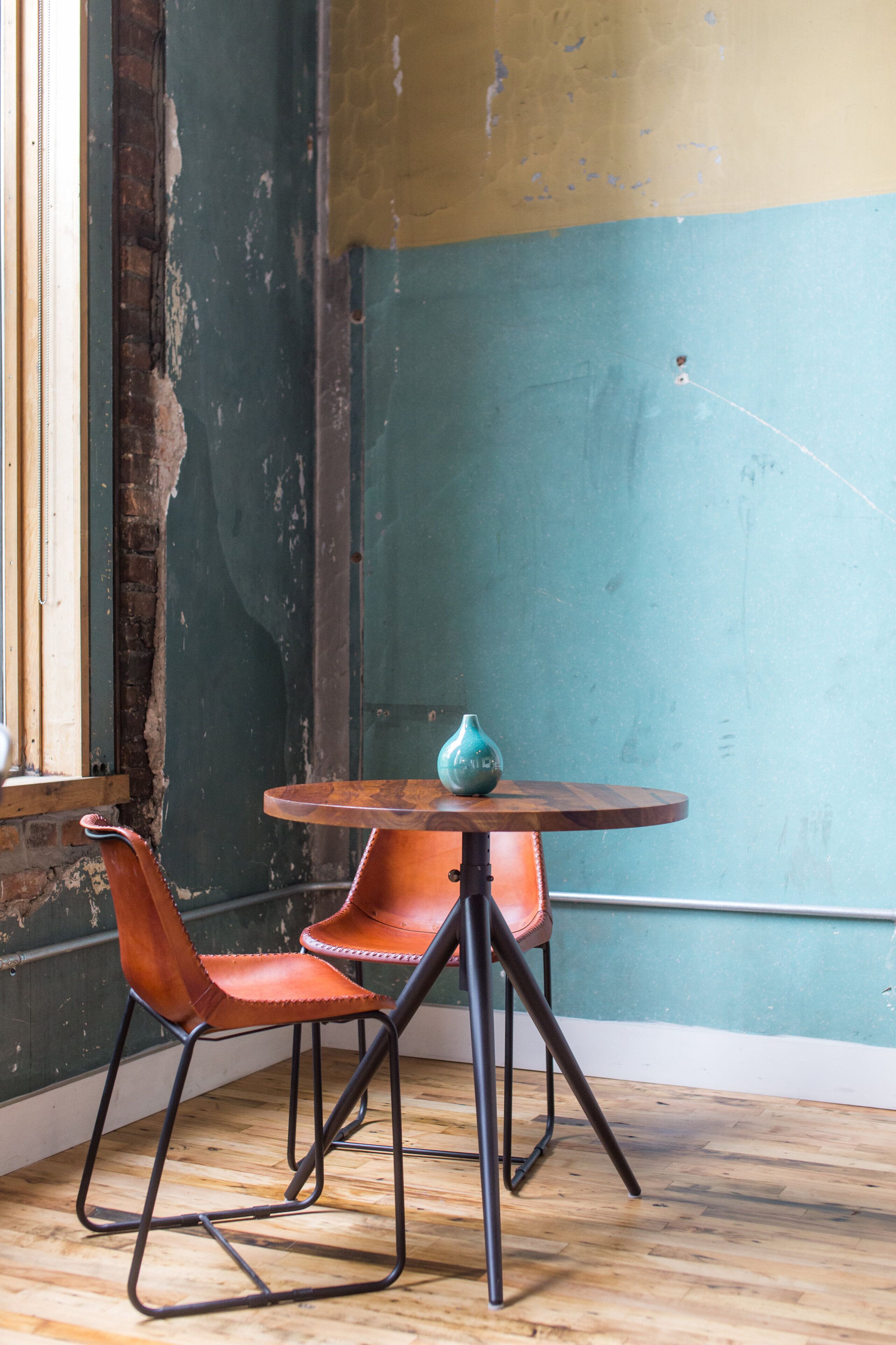 A room with a wooden floor, a round table with a vase, and two leather chairs.