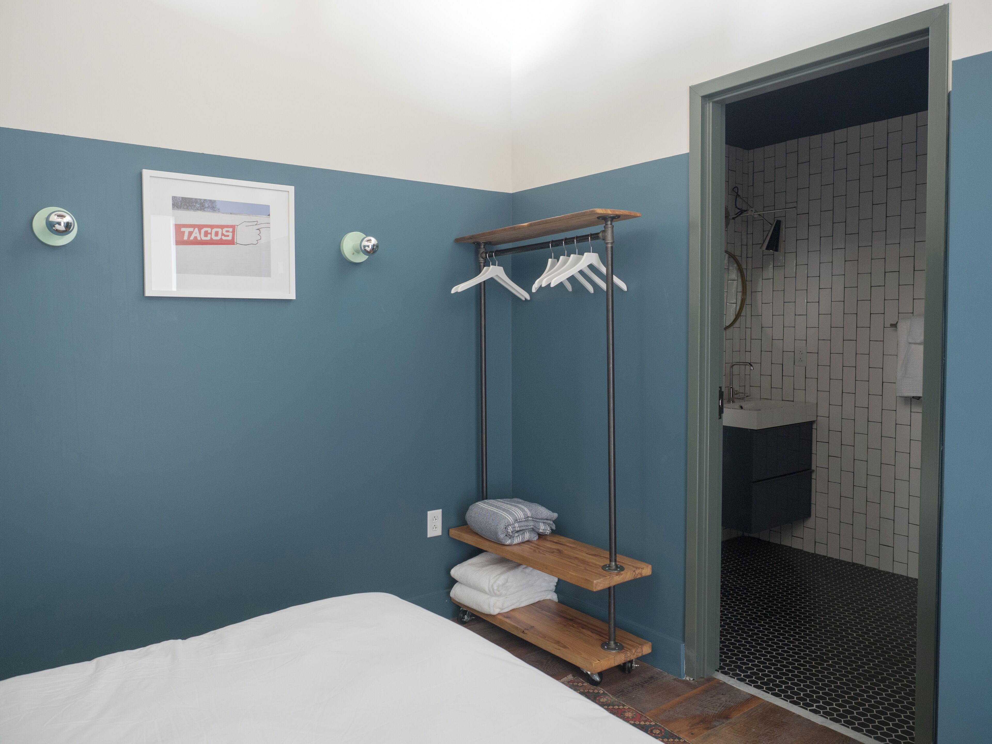 Een slaapkamer met een bed, een wandhanddoekhouder, een ingelijst beeld en een badkamer zichtbaar door een open deur.