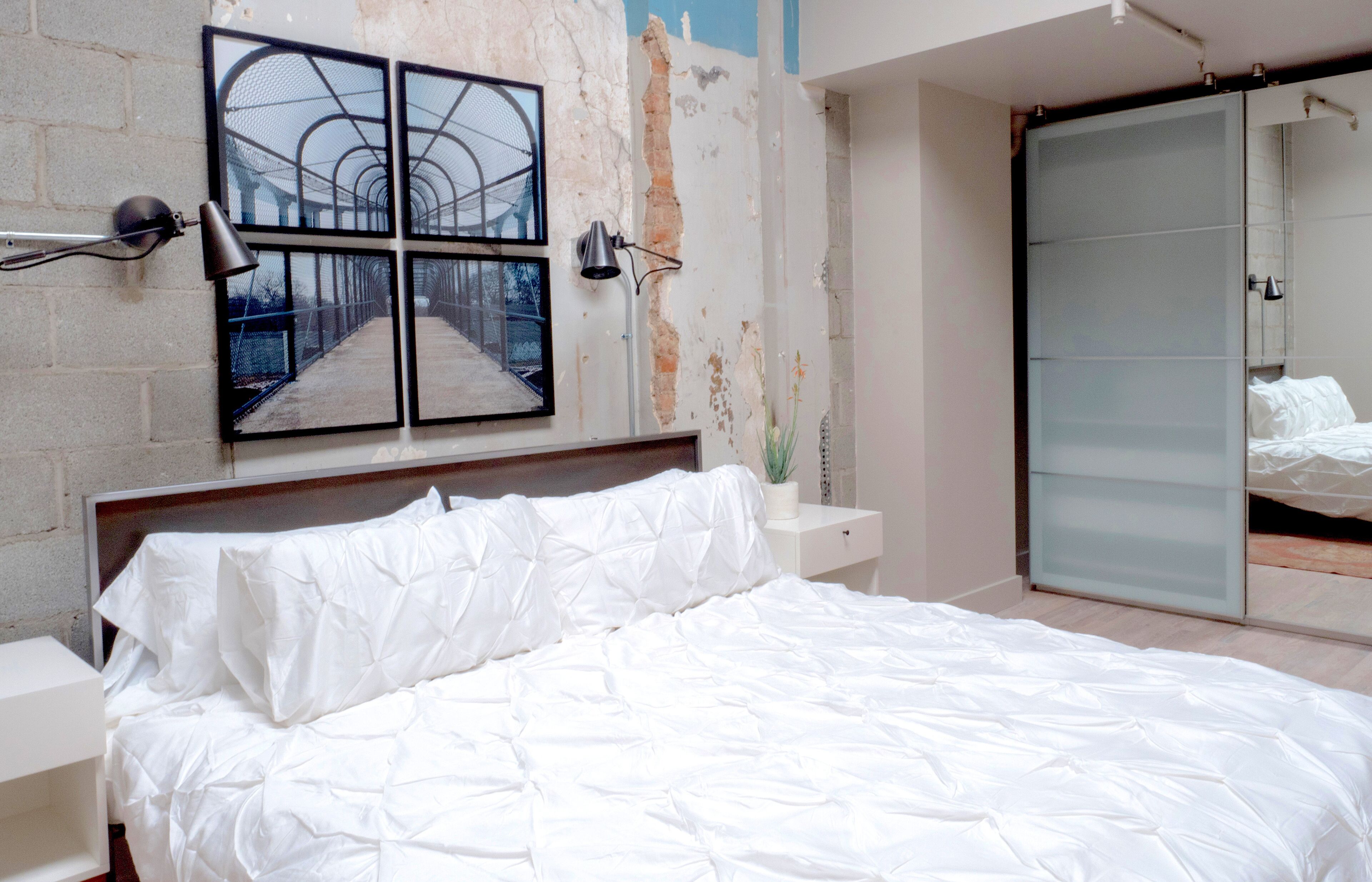 A bedroom with a large bed, a nightstand, a wall-mounted lamp, and a sliding door closet.
