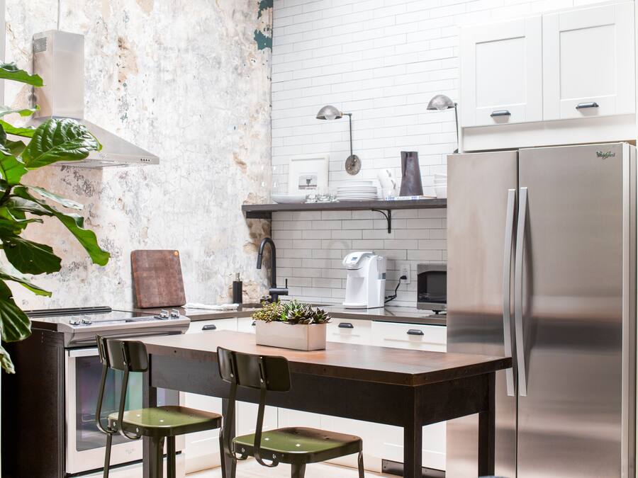 A kitchen with a central island, stainless steel appliances, and a rustic brick wall.