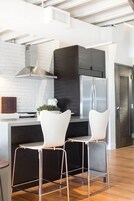 A modern kitchen with a stainless steel refrigerator, white bar stools, and a white brick backsplash.