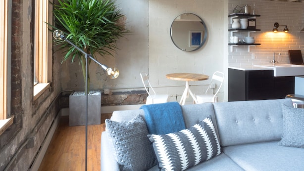 A modern living room with a grey sofa, a round mirror, and a potted plant. - 506 Lofts - Anchor Rentals (Nashville)