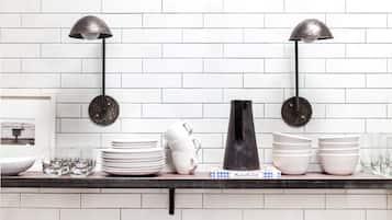 Una encimera de cocina con salpicadero de azulejos blancos, una lámpara de pie negra y diversos utensilios de cocina, incluyendo platos, tazas y un jarrón.