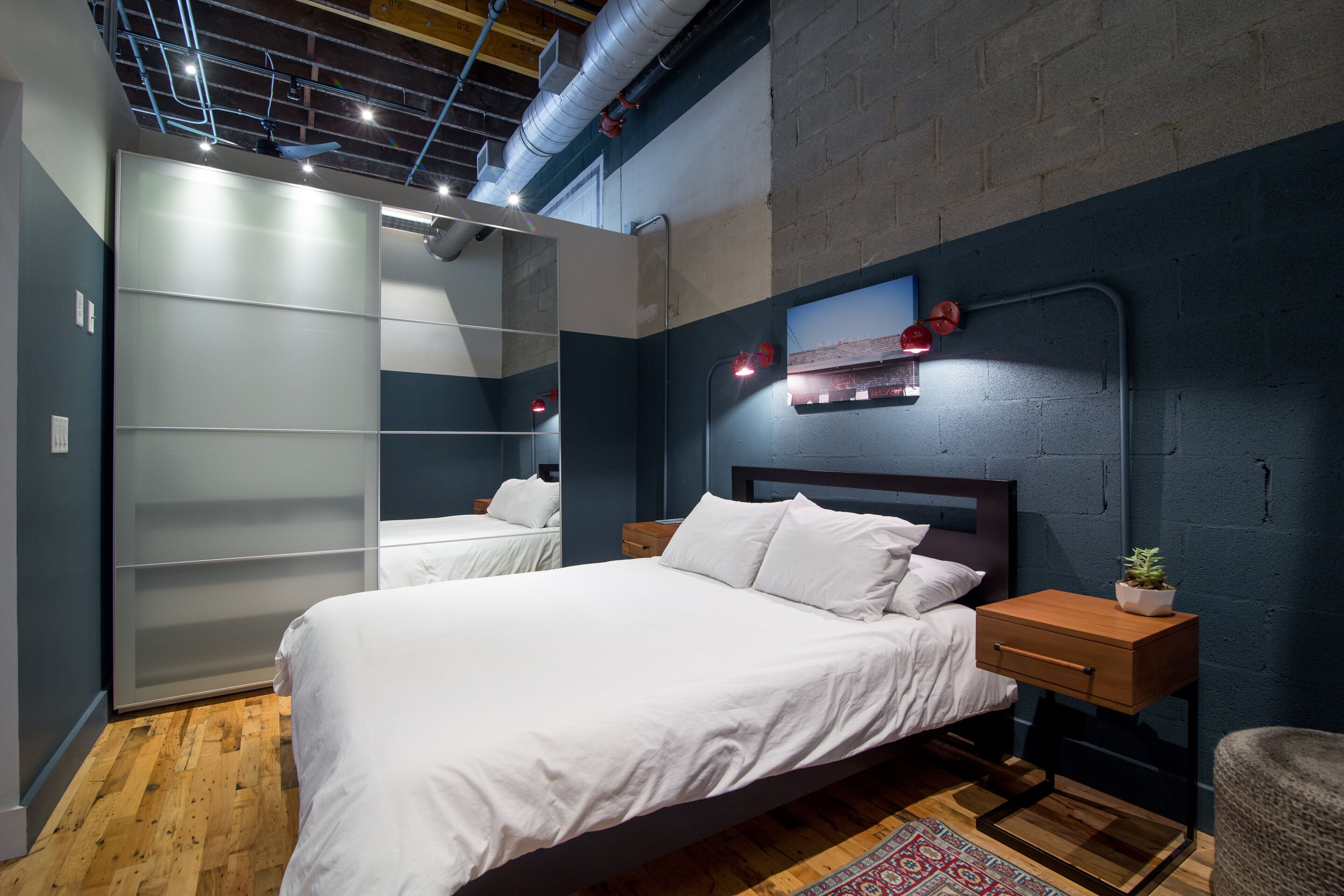 A modern bedroom with a large bed, a wooden nightstand, a mirror, and a built-in wardrobe.