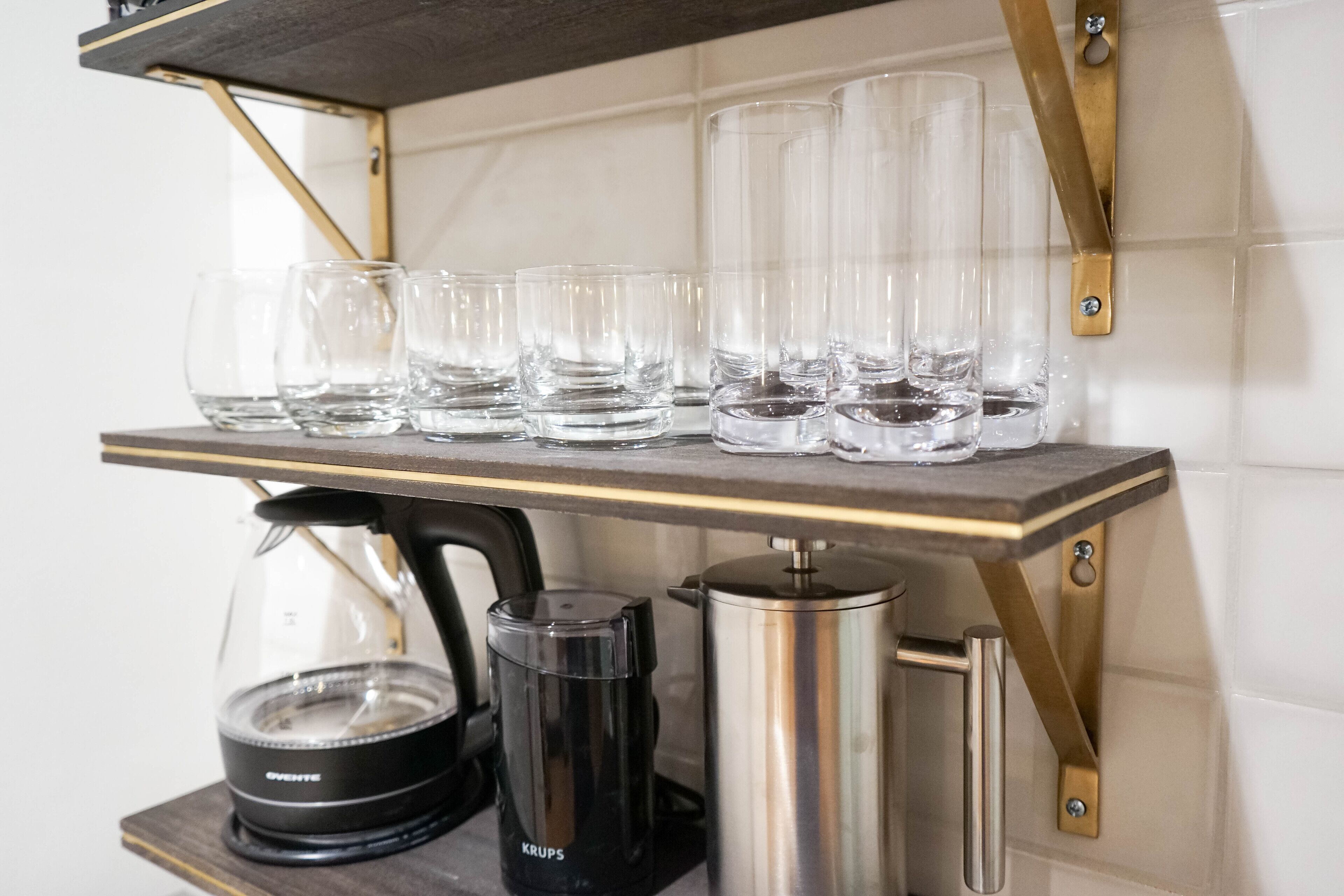 En köksbänk med en kaffebryggare, en vattenkokare och flera glas.