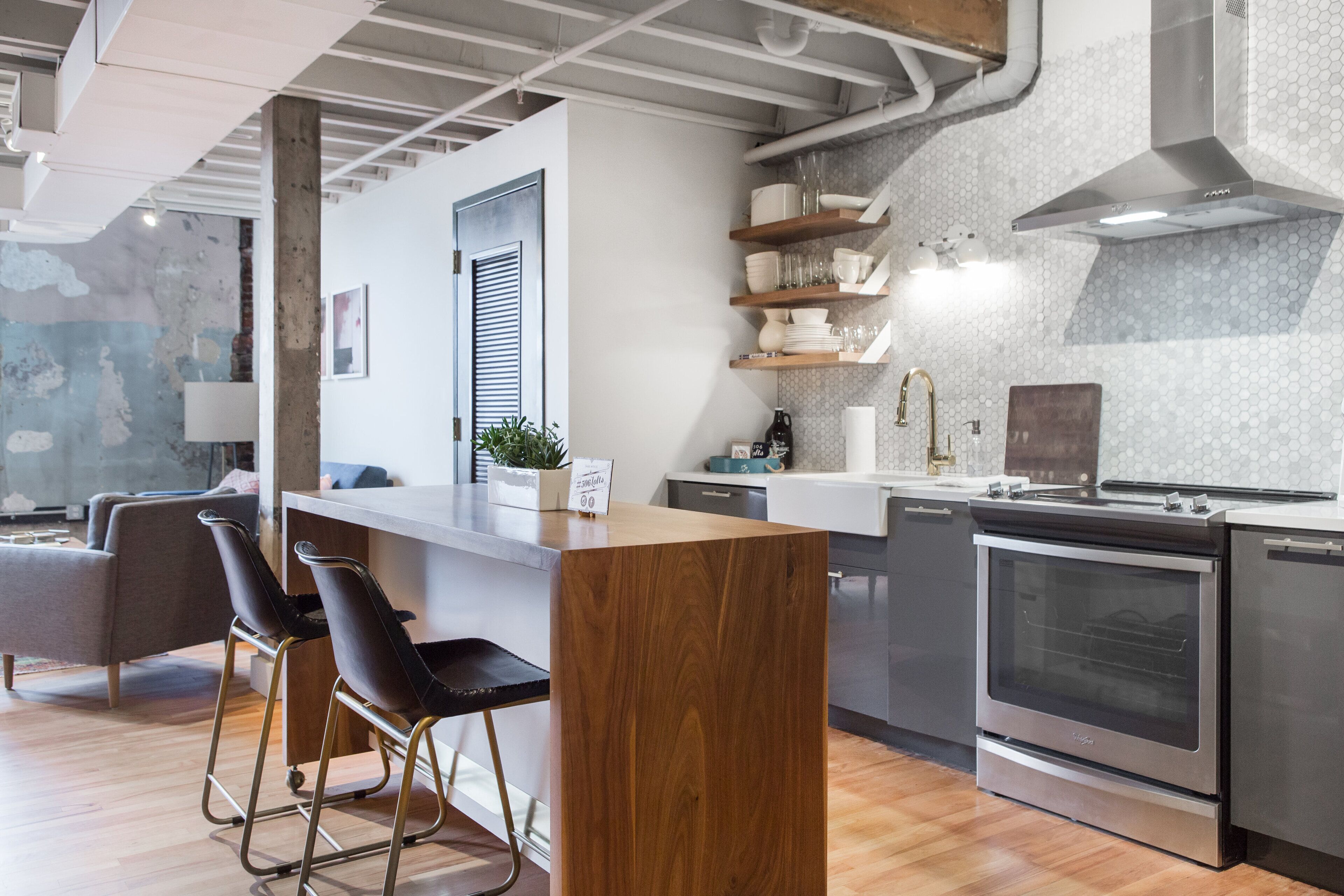 Una cocina moderna con una isla central, taburetes de bar, electrodomésticos de acero inoxidable y un salpicadero de azulejos.