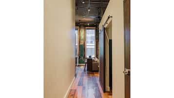 A narrow hallway with wooden flooring, a door on the right, and a window at the end.