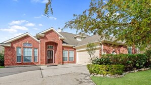 A two-story brick house with a garage, a front yard with a lawn and shrubs, and a clear blue sky. - Beautiful Home, spacious office & Xbox Game Room. (Montgomery County)