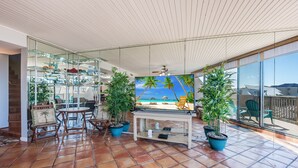 A spacious patio with terracotta tiles, a glass wall with a tropical mural, and potted plants. - Saltwater Dreams @ MP317 | Pools and Beaches (Port Aransas)