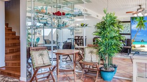 A spacious living area with a wooden staircase, a glass display shelf with decorative items, and a large potted plant. - Saltwater Dreams @ MP317 | Pools and Beaches (Port Aransas)