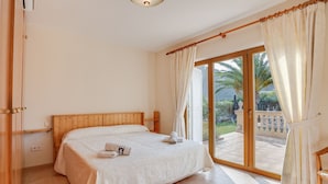 Une chambre avec un lit en bois, un balcon agrémenté de rideaux et une vue sur la verdure.