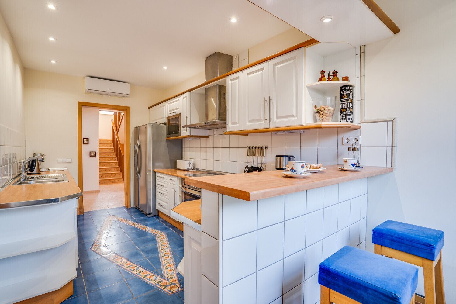 A modern kitchen with white cabinets, a stainless steel refrigerator, and a wooden countertop.