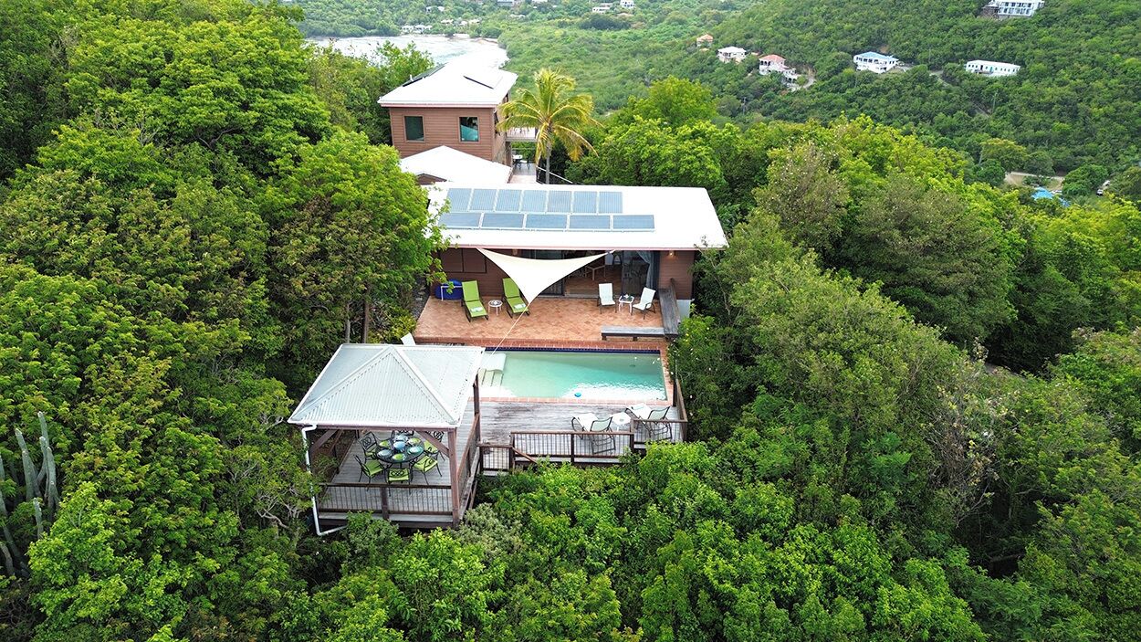 Una casa con piscina rodeada de abundante vegetación, un panel solar en el techo y vistas del paisaje circundante.