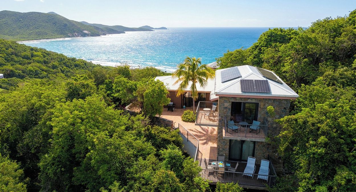 Ein zweistöckiges Haus mit einem Balkon mit Blick auf einen Strand und den Ozean.