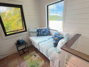 A cozy bedroom with a bed, a small table, and a window with a view of greenery.