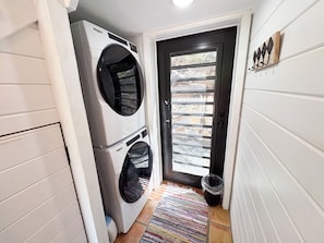 Uma lavanderia com duas máquinas de lavar e secar empilhadas, uma porta com janela e um pequeno tapete no chão.
