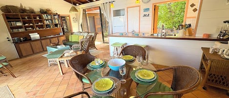Un coin repas avec des chaises en osier, une table en verre et une cuisine en arrière-plan.
