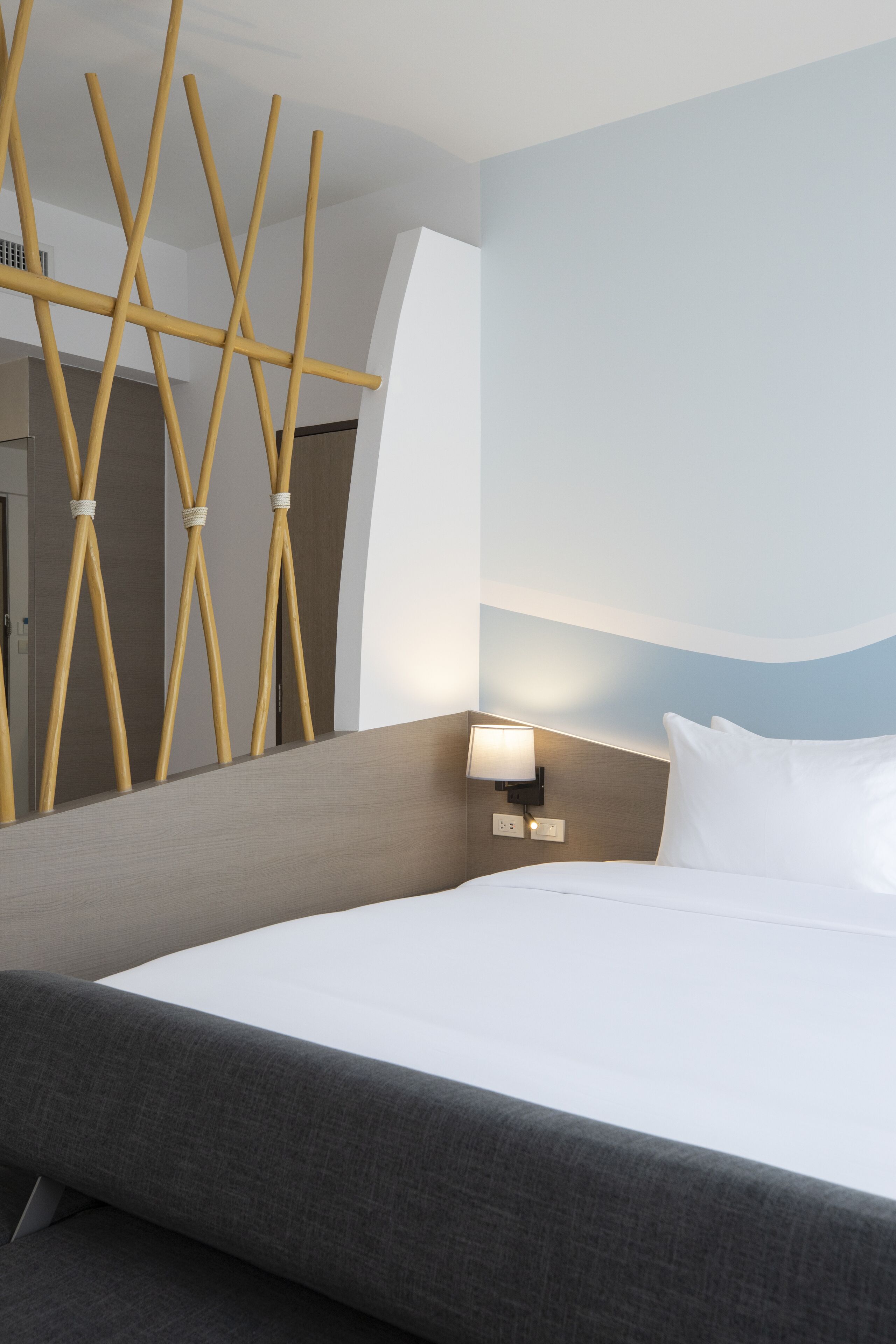 Habitación de hotel con cama, mesita de noche con lámpara, luz empotrada en la pared y un panel decorativo de madera.