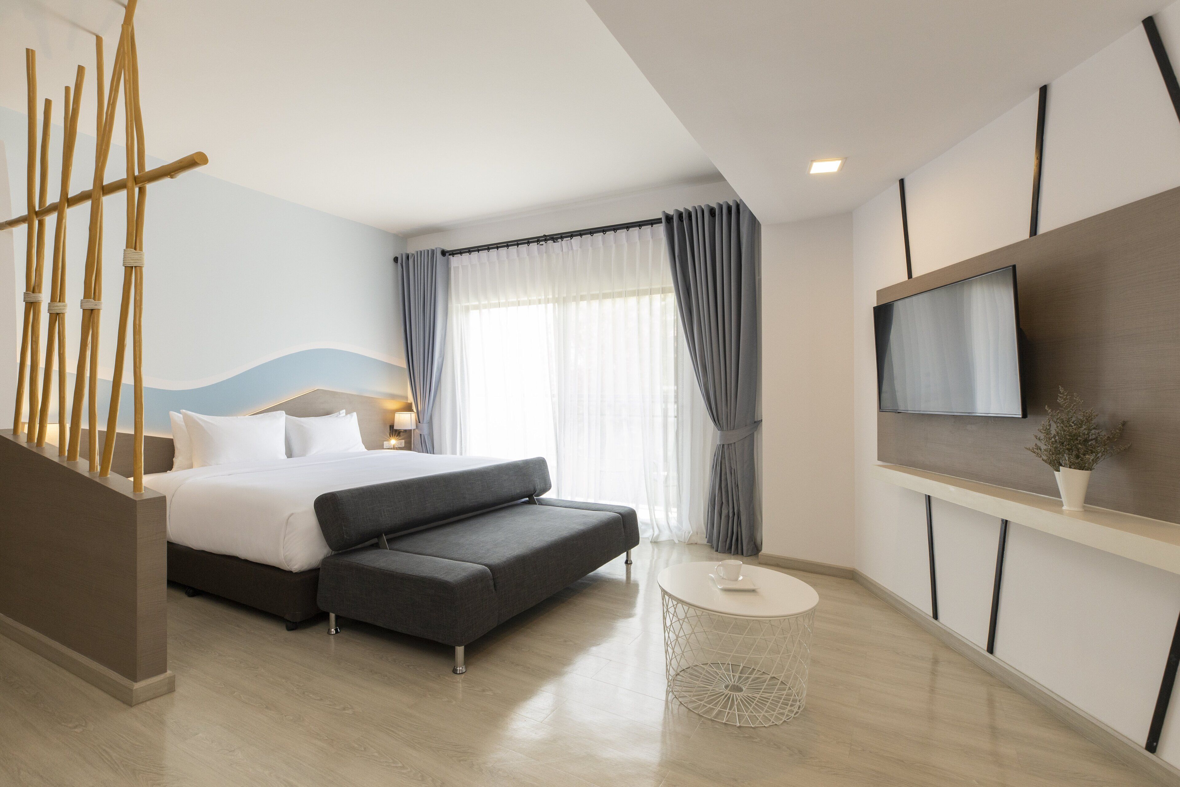 A modern hotel room with a bed, sofa, TV, and a small round table.