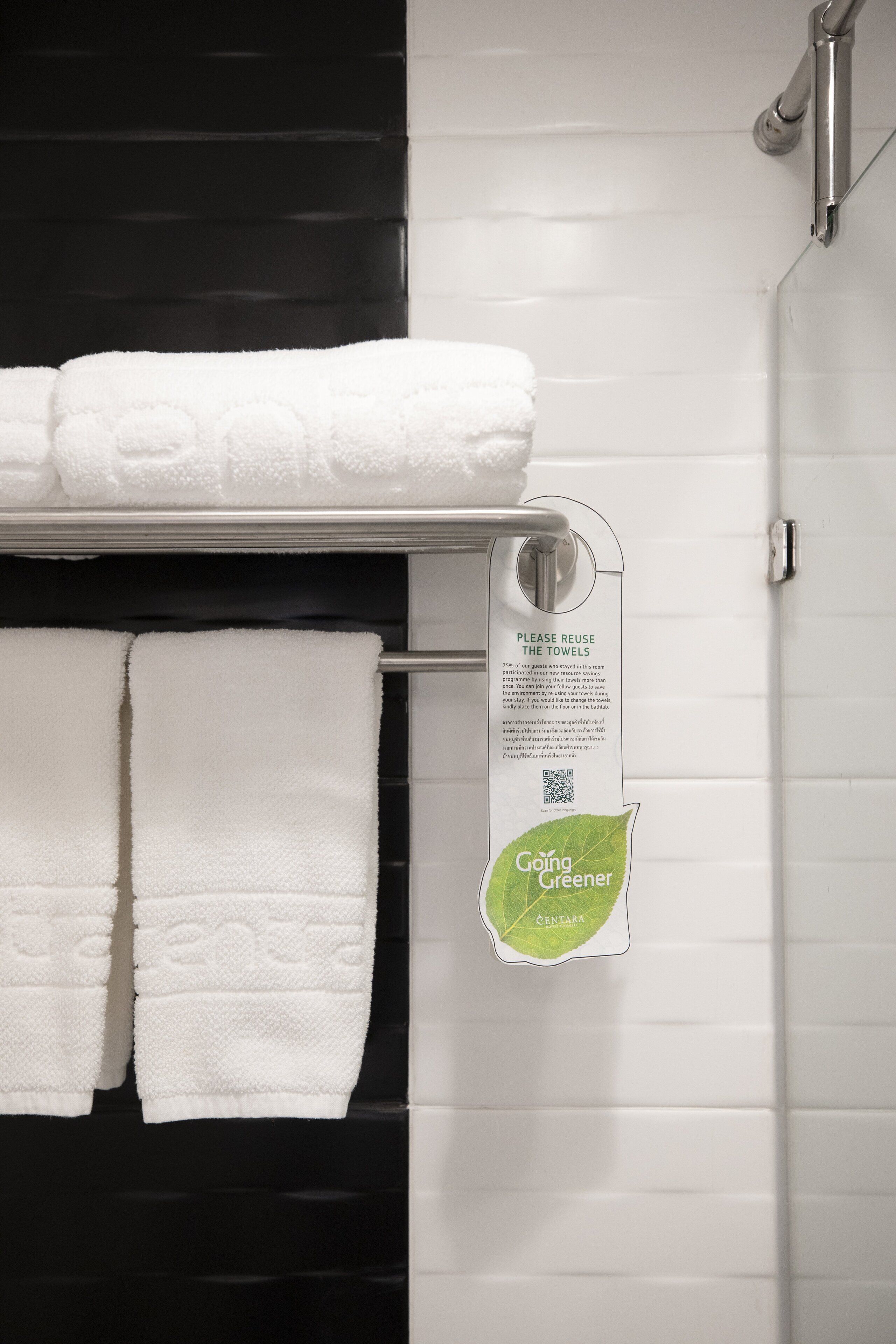 A bathroom with white towels hanging on a rack, a QR code, and a sign encouraging towel reuse.