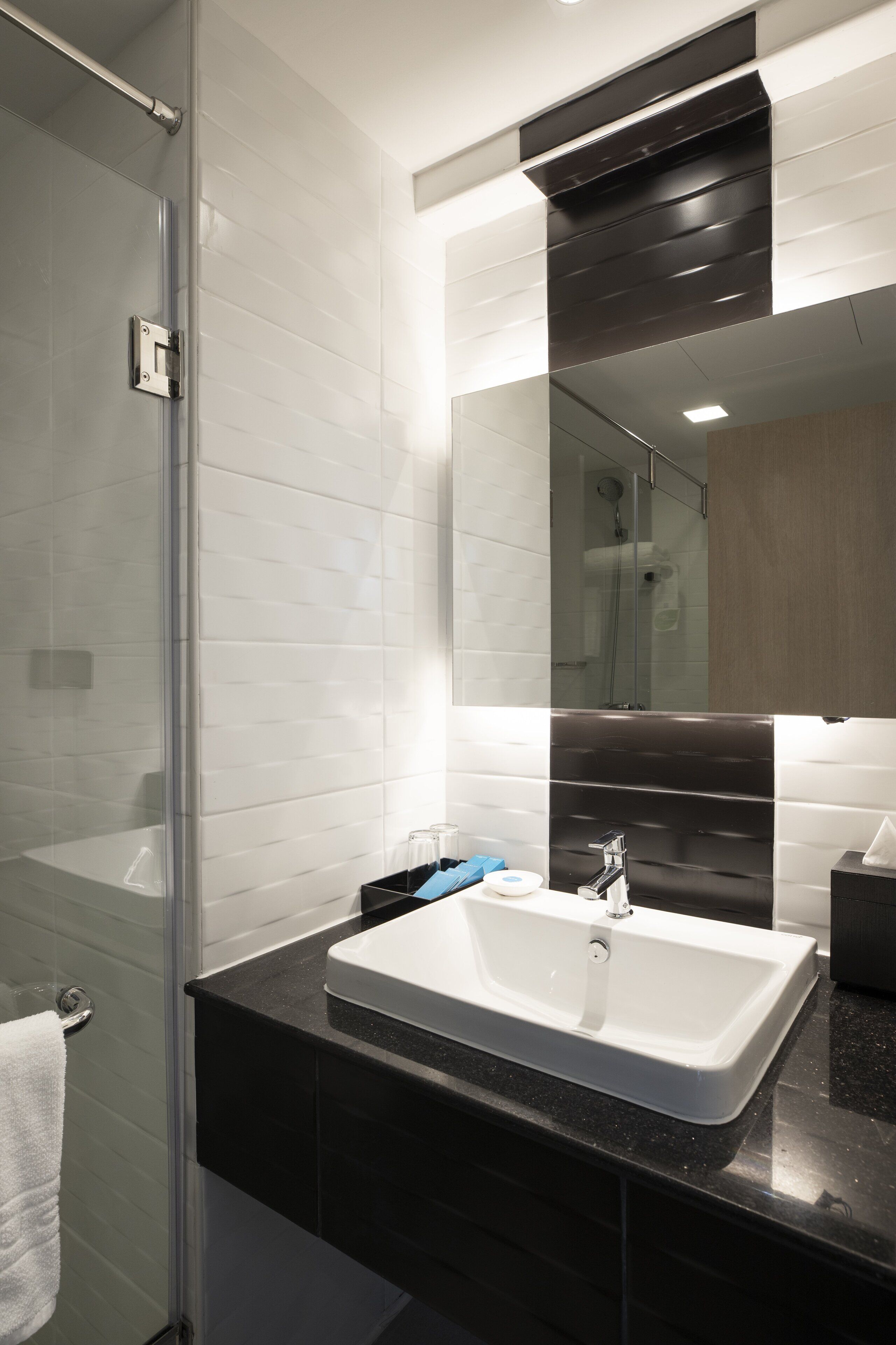 Un baño moderno con cabina de ducha de vidrio, un lavabo blanco y un espejo grande.