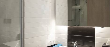 Un baño moderno con cabina de ducha de vidrio, un lavabo blanco y un espejo grande.
