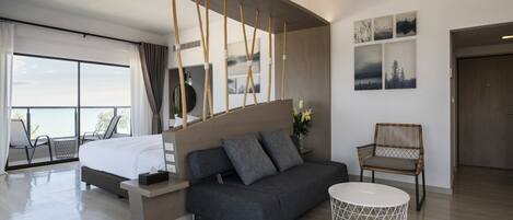Une chambre d’hôtel moderne avec un lit, un canapé et une petite table ronde. Elle dispose d’un balcon avec vue et est dotée d’un plafond en bois et de décorations murales.