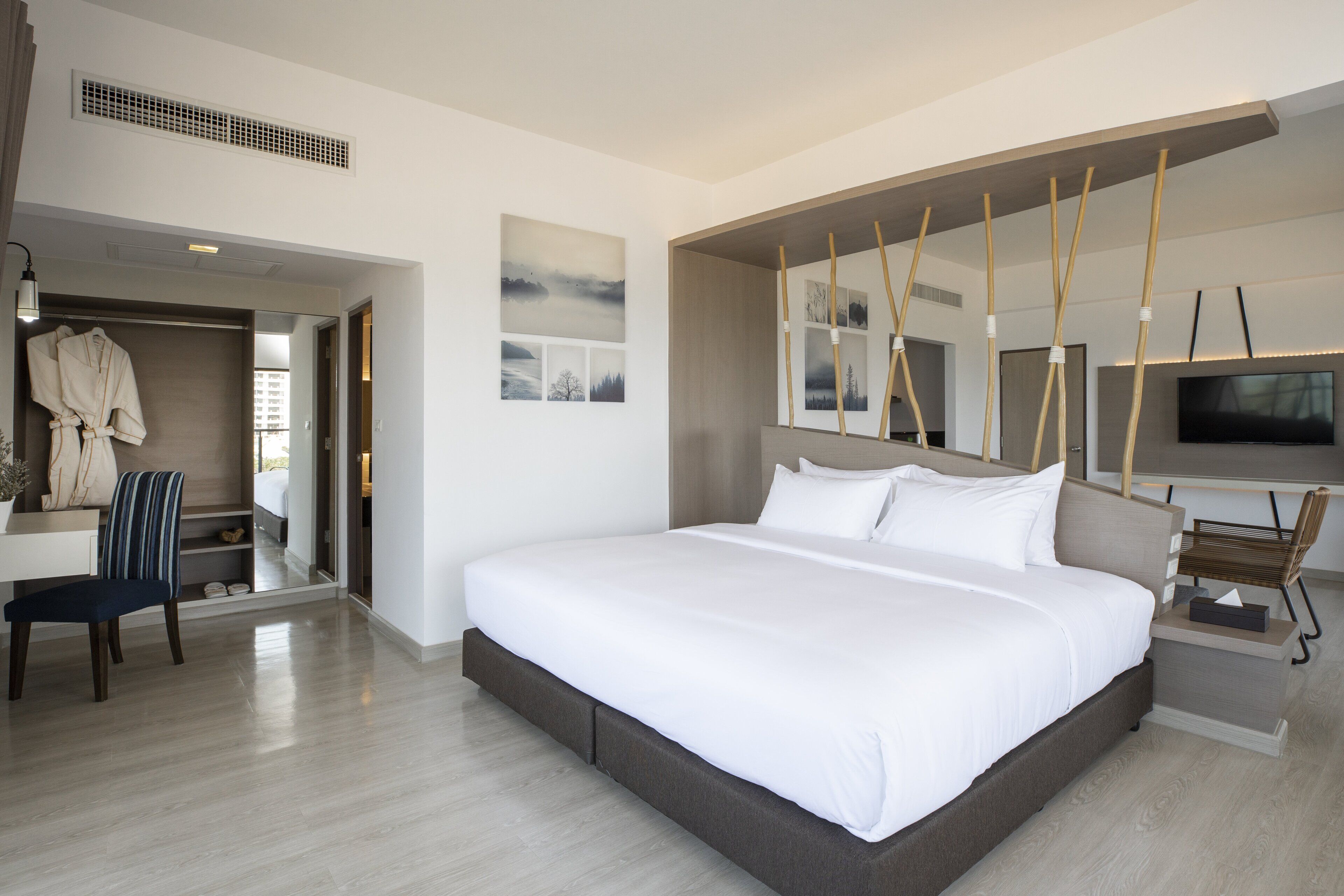 A modern hotel room with a large bed, a desk, a chair, and a TV.