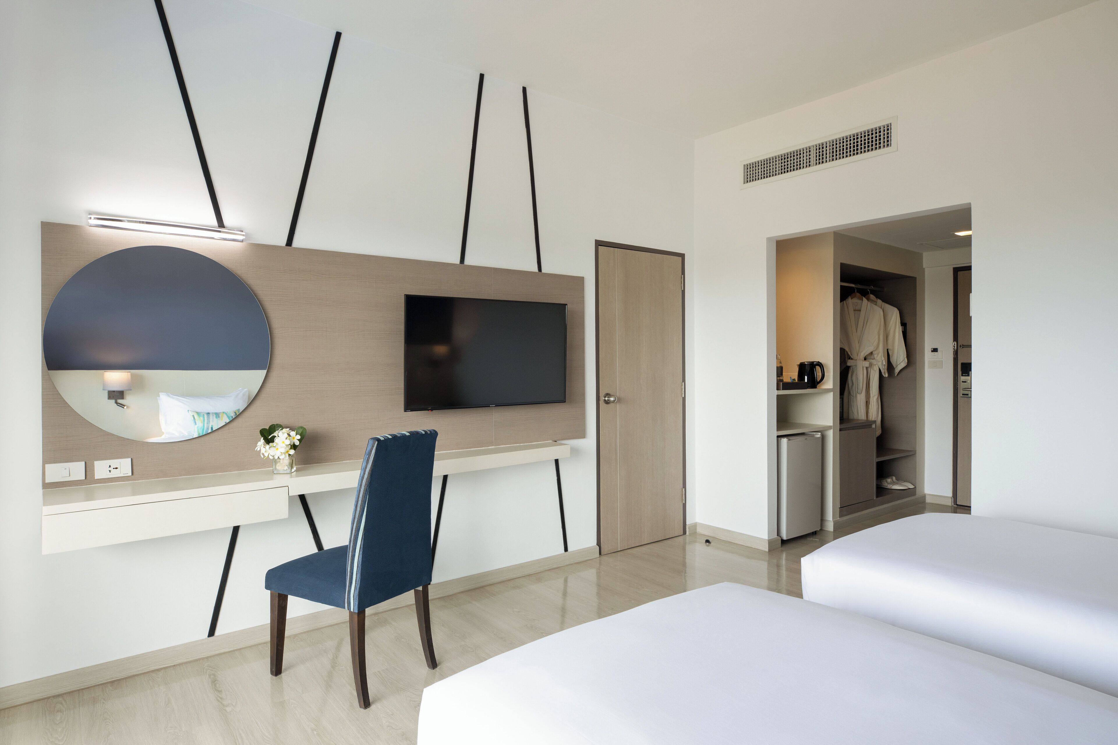 A modern hotel room with a desk, chair, TV, and two beds.