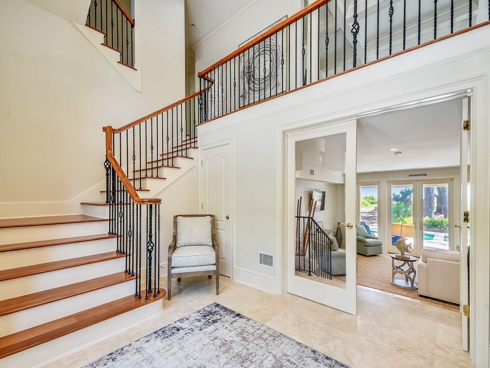 A multi-level home interior with a wooden staircase, a chair, and a view into a living area.