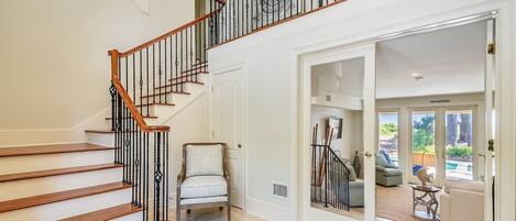A multi-level home interior with a wooden staircase, a chair, and a view into a living area.