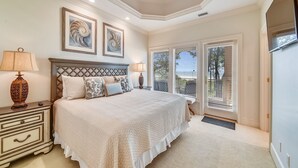 A bedroom with a large bed, a ceiling fan, and a view of the outdoors through the windows. - Luxurious Ocean Front Home w/ Rec Room (Hilton Head Island)