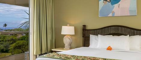 A hotel room with a large bed, a nightstand with a lamp, a painting on the wall, and a view of greenery outside.