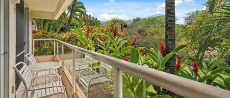 A balcony with white chairs and a table, surrounded by lush tropical plants and a view of the landscape.