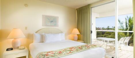 A hotel room with a bed, two bedside lamps, a ceiling fan, a painting on the wall, and a balcony with a table and chairs.
