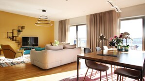 A modern living room with a sofa, TV, dining table, and chairs. - Sea view Apartment Hermes (Budva)
