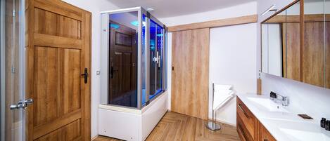 Un baño moderno con suelo de madera, cabina de ducha de cristal, lavabo blanco y tocador de madera.