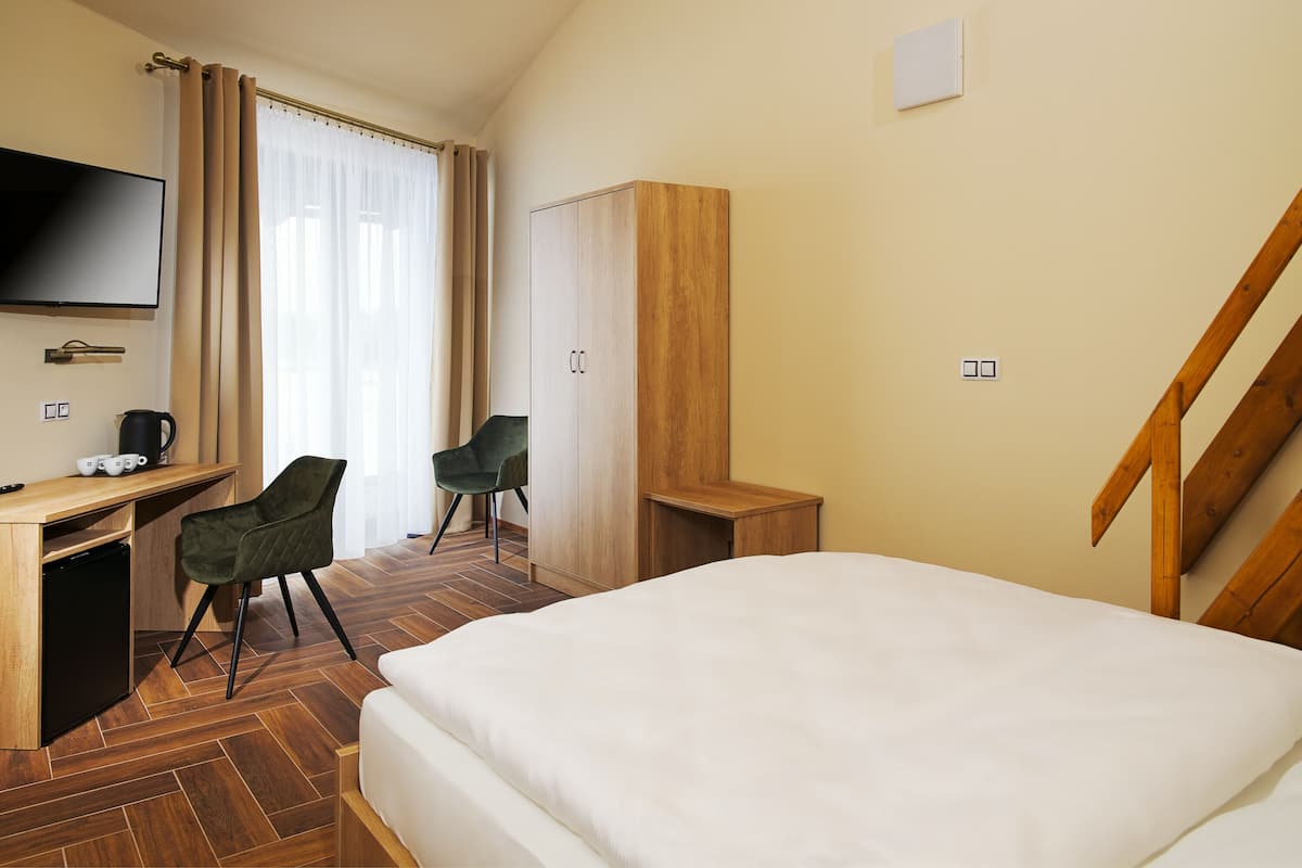 A hotel room with a bed, a desk with a television, two chairs, a wardrobe, and a staircase.