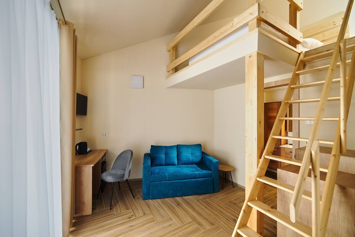 A compact room with a bunk bed, a desk with a chair, and a blue sofa.