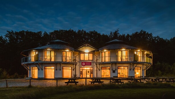 A three-story resort building with a central entrance, outdoor seating, and a sign indicating it is a resort. - Hotel Dymník (Rumburk)