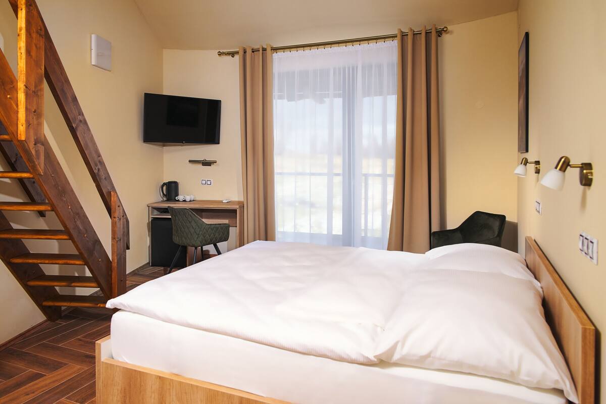 A bedroom with a bed, a desk, a chair, a television, and a staircase.