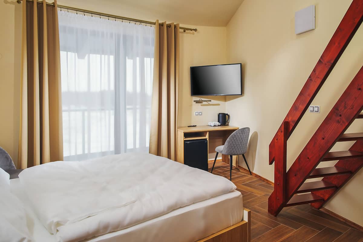 A hotel room with a bed, a desk with a chair, a television, and a wooden staircase.