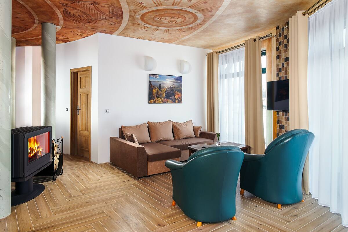 A living room with a fireplace, sofa, teal chairs, and a TV.