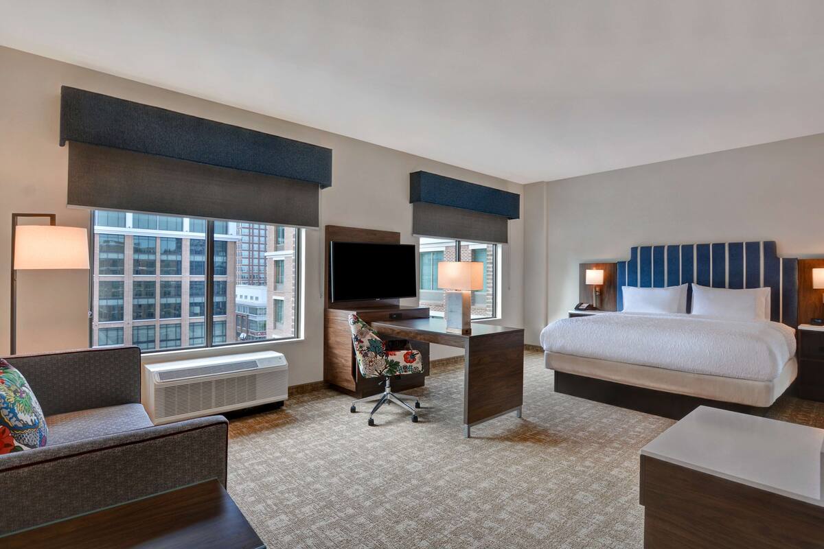 A hotel room with a large bed, a desk with a TV, a chair, and a couch.