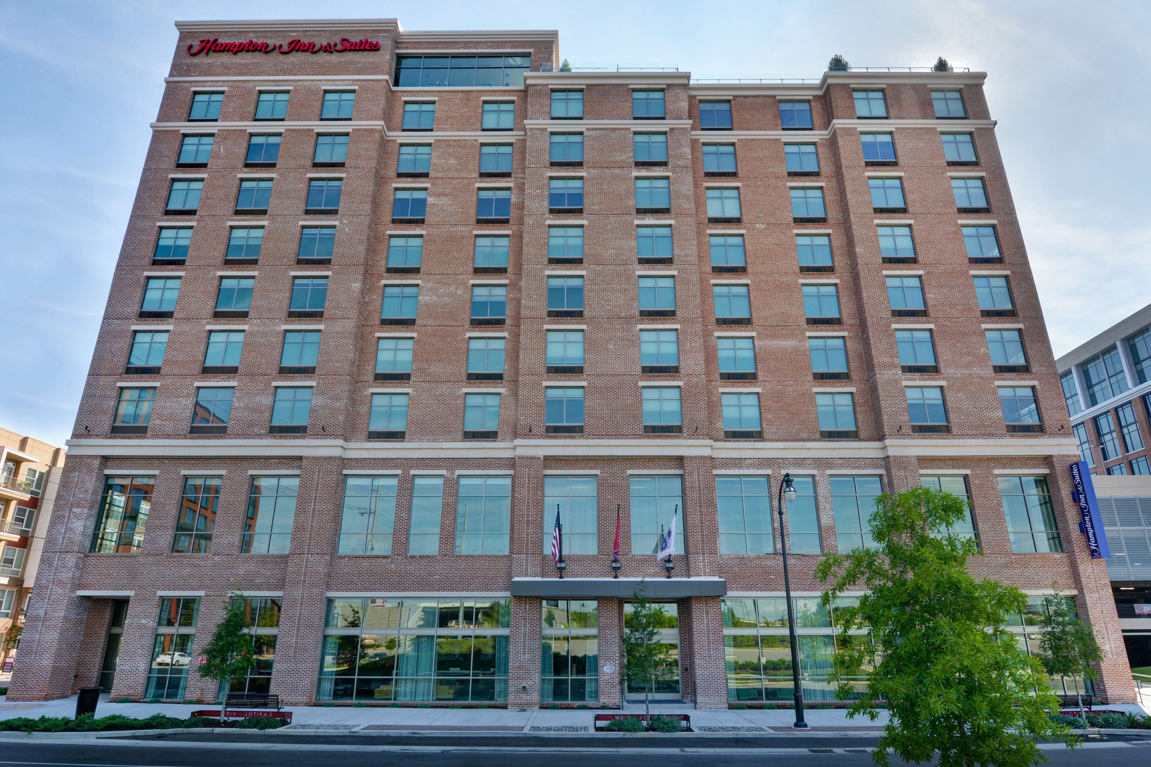 A multi-story hotel with a brick facade, large windows, and a sign reading "Hampton Inn & Suites."