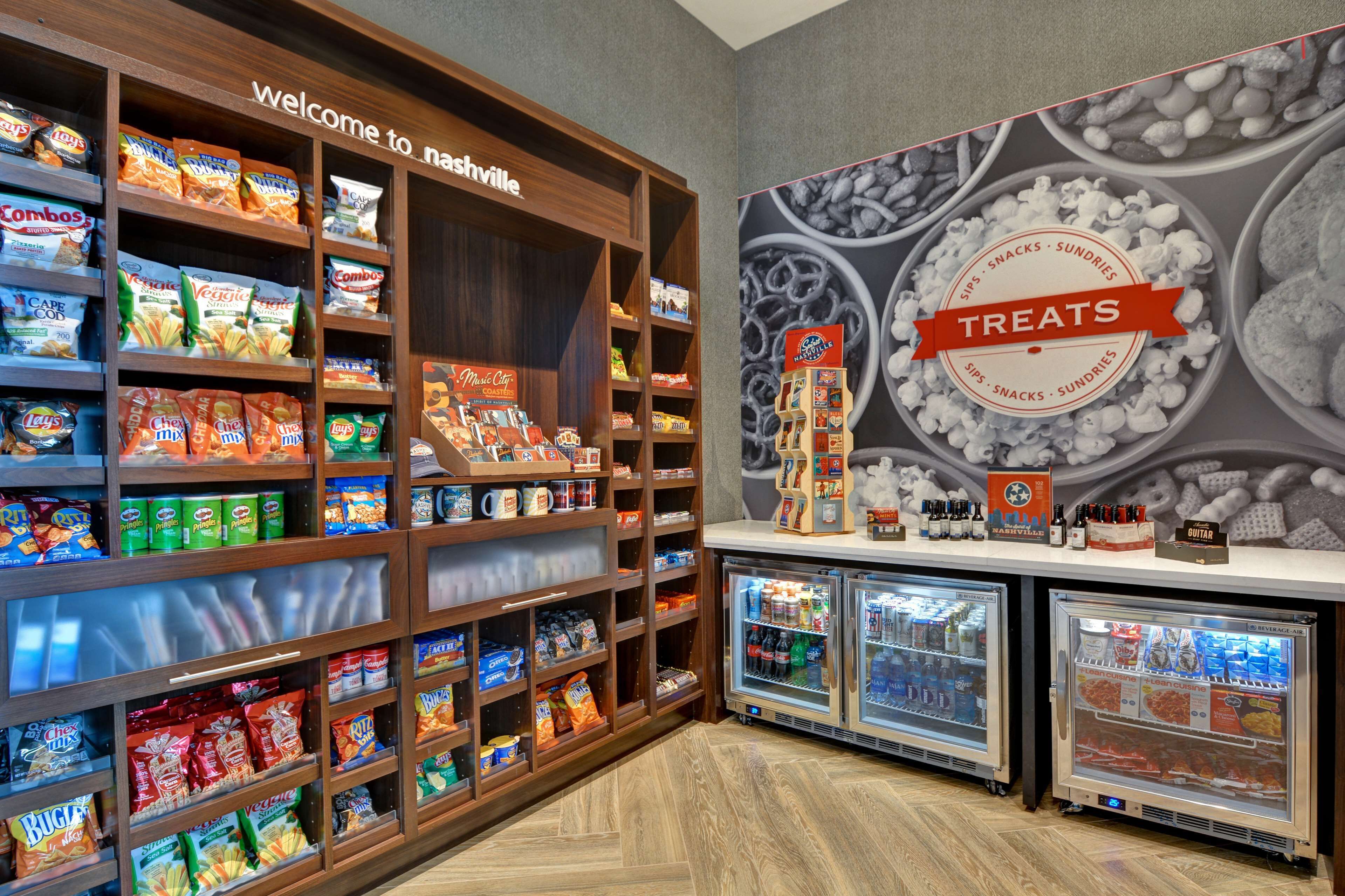 Un espace dédié aux collations et aux produits gourmands, avec des étagères remplies de diverses sortes de snacks et une pancarte indiquant « Bienvenue à Nashville ».