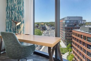 A modern office space with a large window, a wooden desk, a green chair, and a lamp.