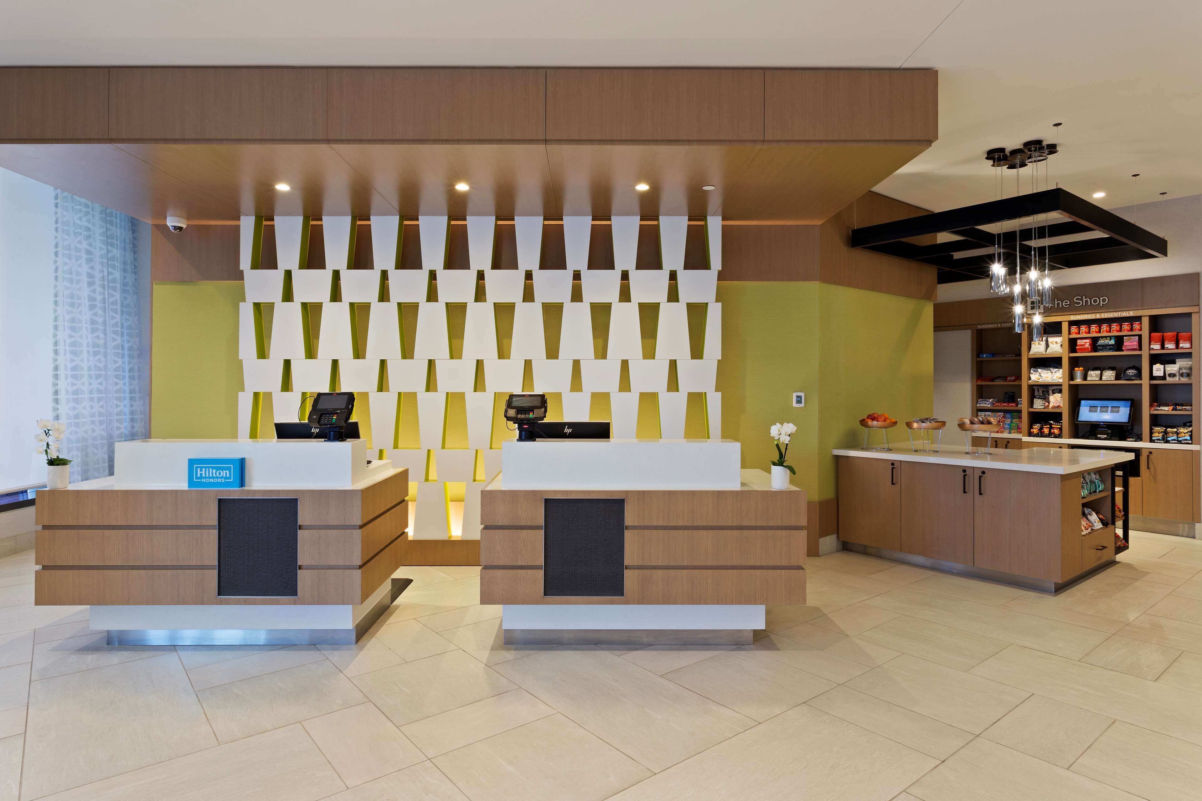 Zona de recepción de un hotel con dos mostradores, un panel decorativo y una tienda al fondo.