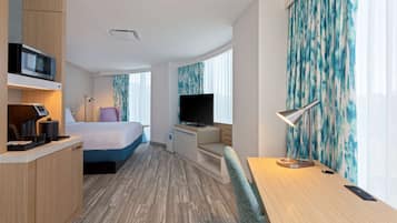 A hotel room with a bed, a desk, a TV, a microwave, and a small kitchenette.